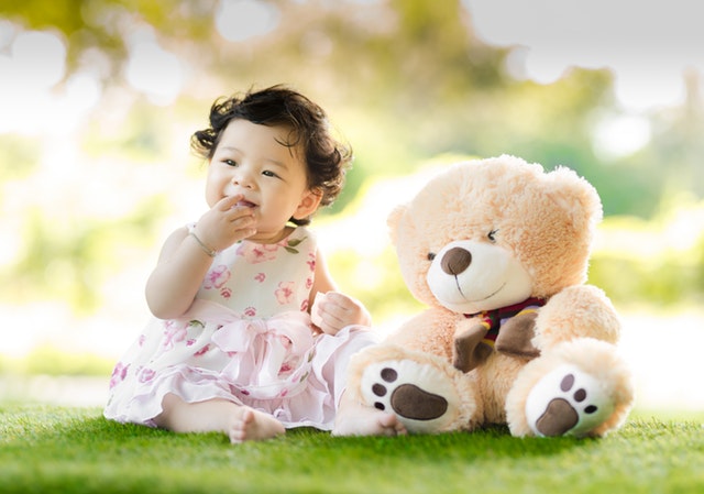 dítě sedící na trávě s plyšovým medvědem